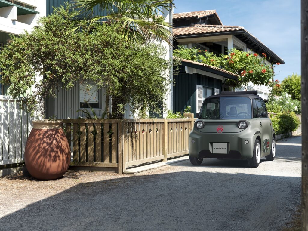 Citroën Ami Outdoor in Khaki-Grün vor einem Holzzaun in einer Gasse
